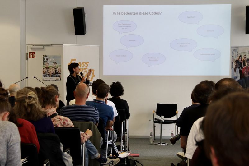 Menschen in einem Seminarraum. Vorne wird eine Präsentation gezeigt.