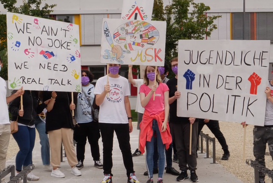 Abbildung zeigt mehrere Personen, die Transparente (Banner) hochhalten.