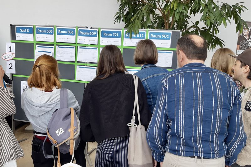 Menschen stehen vor einer Tafel und schauen auf verschiedene Listen.