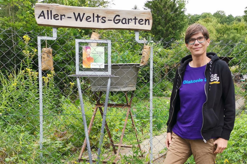 Respekt Coach Melanie Franz steht neben einem Schild mit der Aufschrift Aller-Welts-Garten.