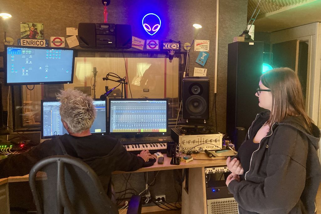 Zwei Personen in einem Tonstudio. Vor ihnen stehen mehrere Bildschirme.