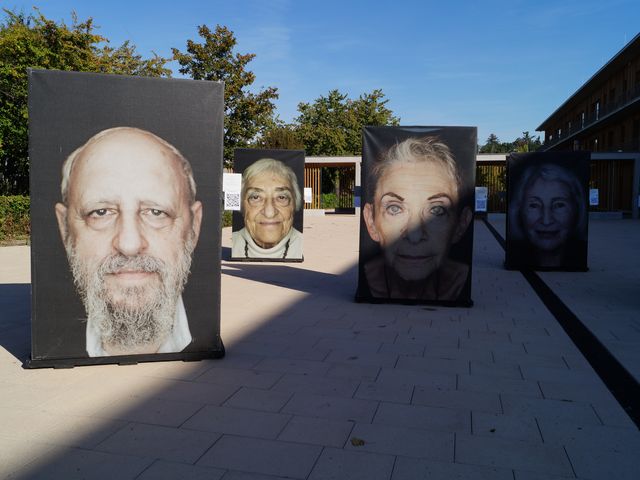 Drei große Porträts von Holocaust-Überlebenden sind im Vordergrund.