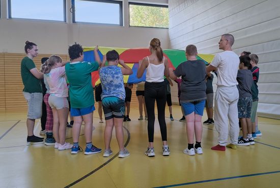 Jugendliche stehen in einem Kreis und halten gemeinsam ein rundes Schwungtuch.