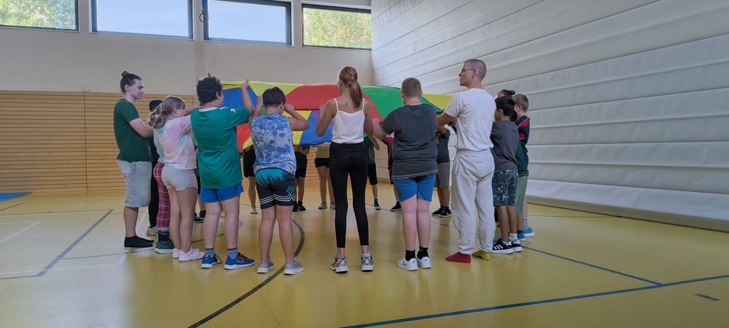 Jugendliche stehen in einem Kreis und halten gemeinsam ein rundes Schwungtuch.