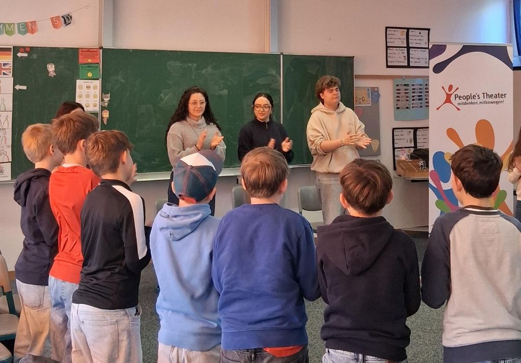 Drei Fachkräfte des People's Theaters stehen im Kreis mit teilnehmenden Kindern und klatschen in die Hände.