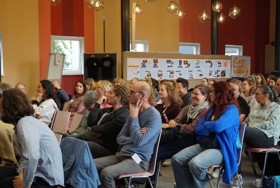 Die Gäste der Veranstaltung sitzen in einem Saal und blicken zur Bühne.