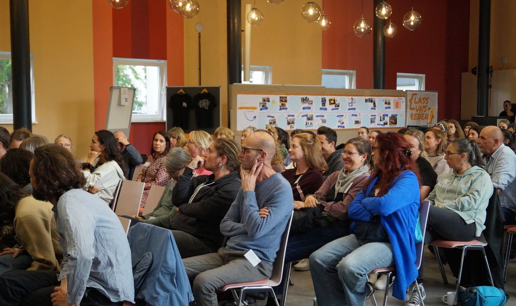 Die Gäste der Veranstaltung sitzen in einem Saal und blicken zur Bühne.