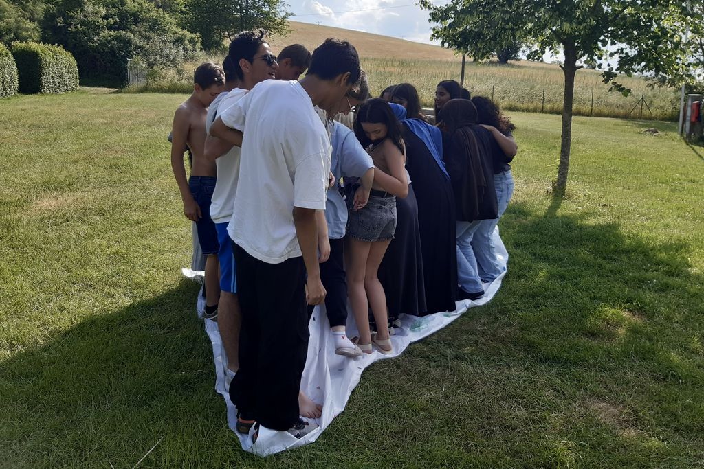 Eine Gruppe junger Menschen steht eng beieinander auf einem Teppich draußen auf einer Wiese.