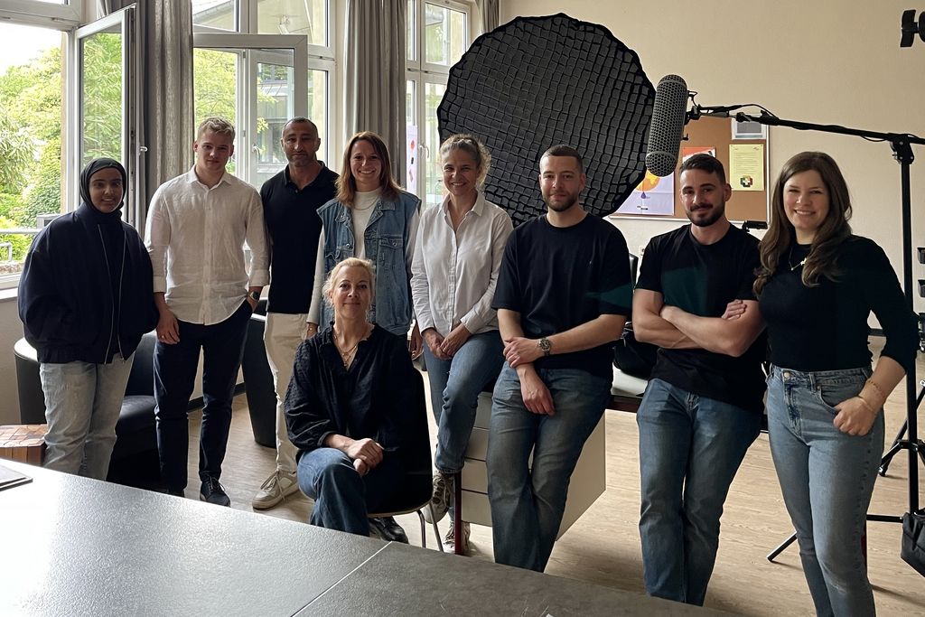 Eine Gruppe Menschen steht in einem Klassenraum. Im Hintergrund ist Filmtechnik zu erkennen.