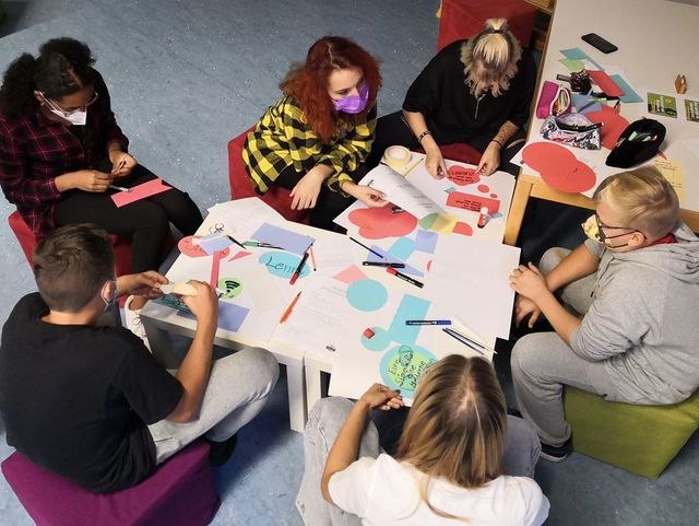 Mehrere junge Personen sitzen am Tisch und kleben kleine Zettel auf ein Flipchart-Papier.