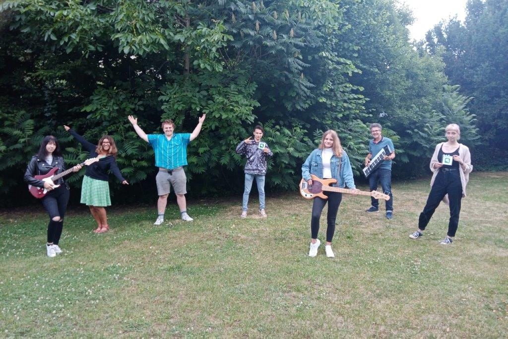 Mehrere junge Personen stehen auf einer Wiese, zwei junge Mädchen spielen Gitarre und ein Junge Keyboard.