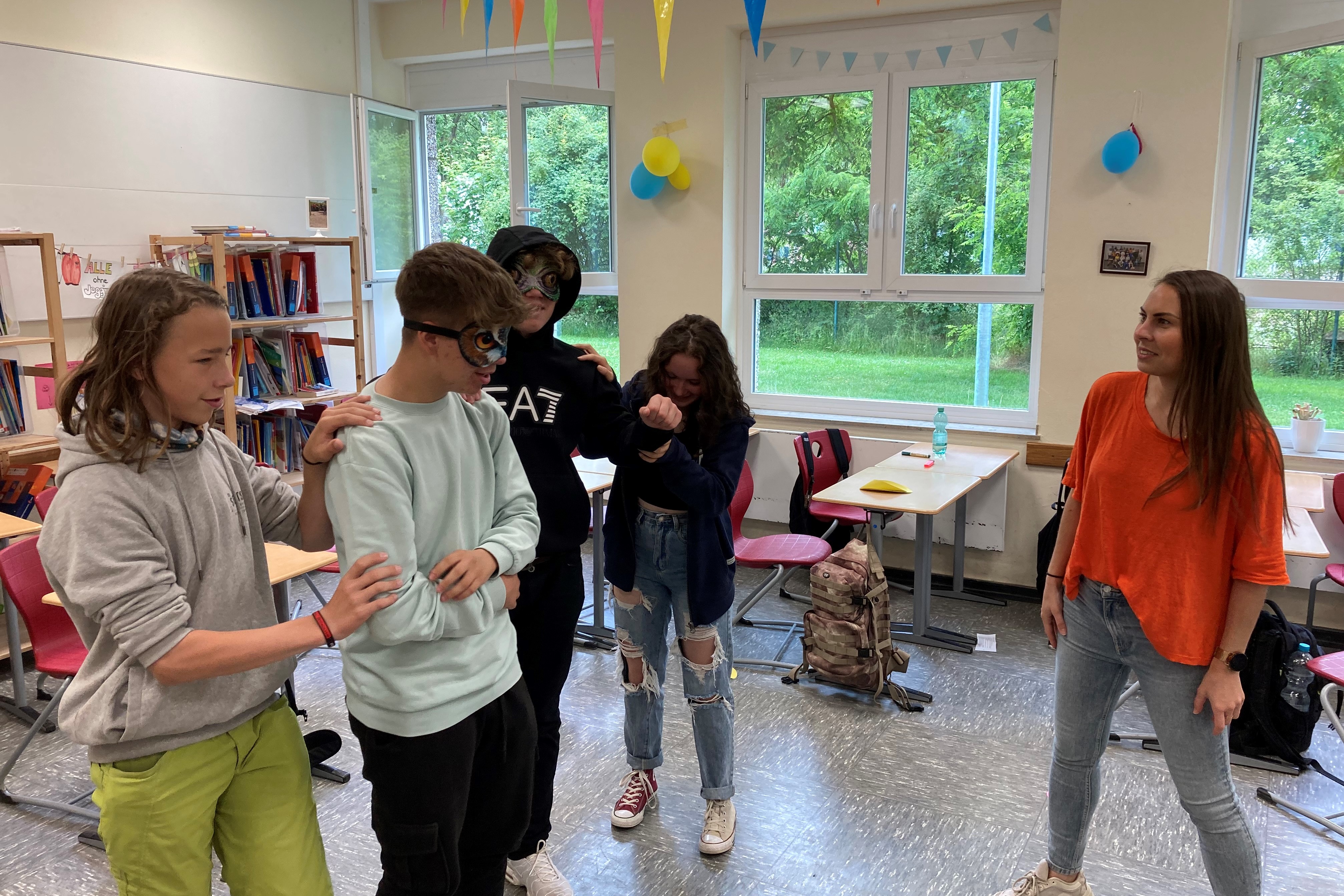 Abbildung von vier jungen Personen, die zusammen vor einer weiblichen Person stehen.