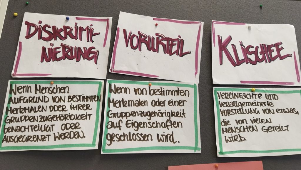 An der Leinwand befestigte Zettel mit der Aufschrift Diskriminierung, Vorurteil und Klischee.