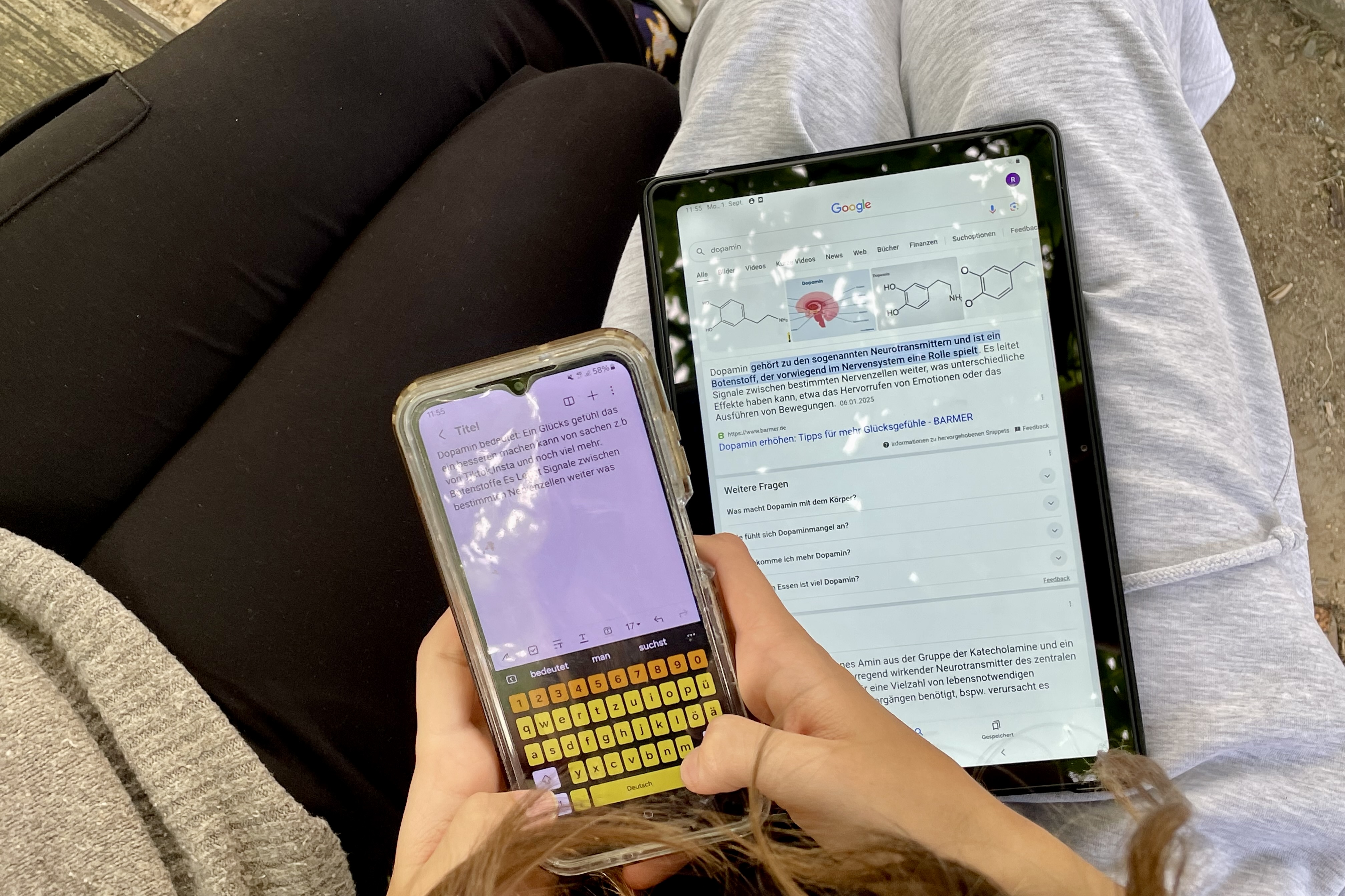 Hände mit Tablet und Handy sind zu sehen. Sie tippen etwas in das Handy.